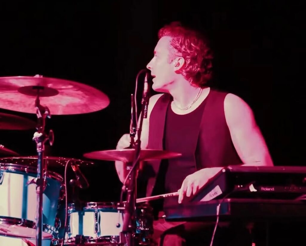 Drummer performing on stage with instruments.